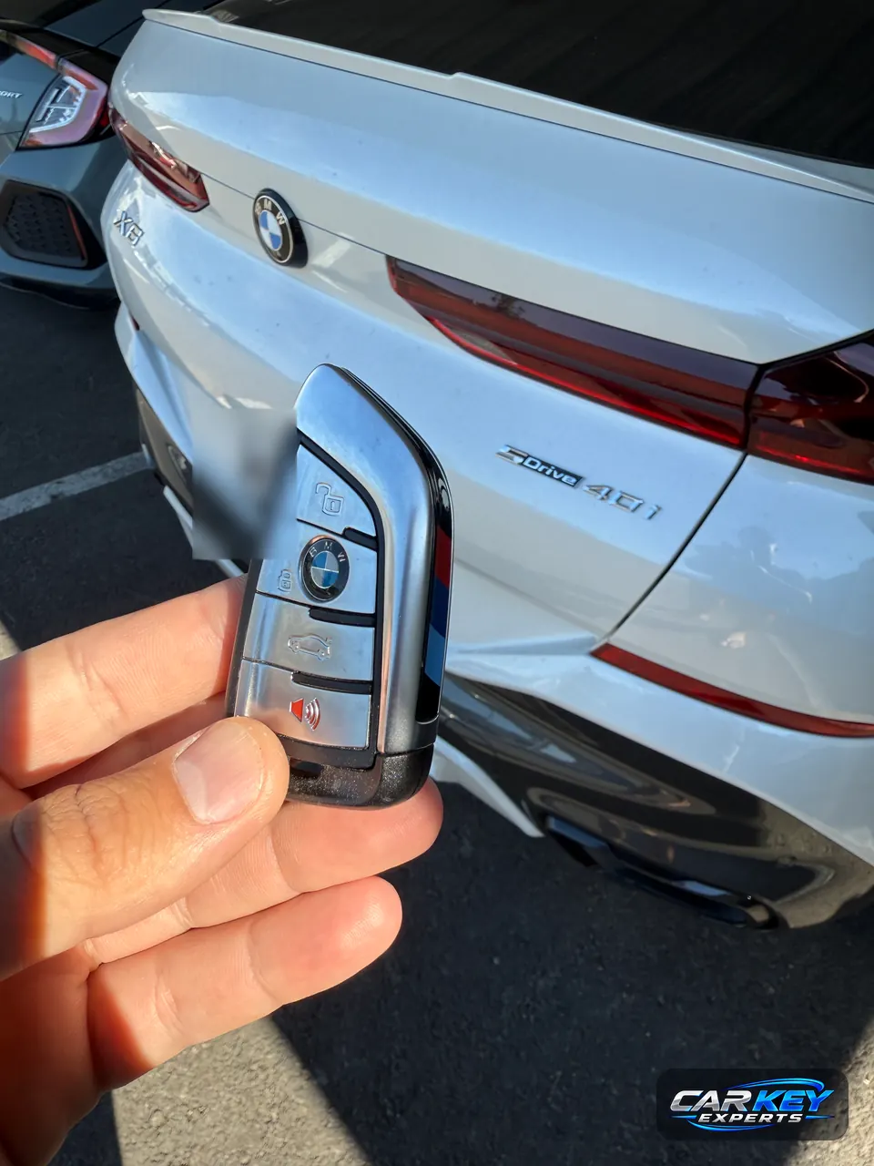 A chrome BMW smart key held at the back of a white BMW X6