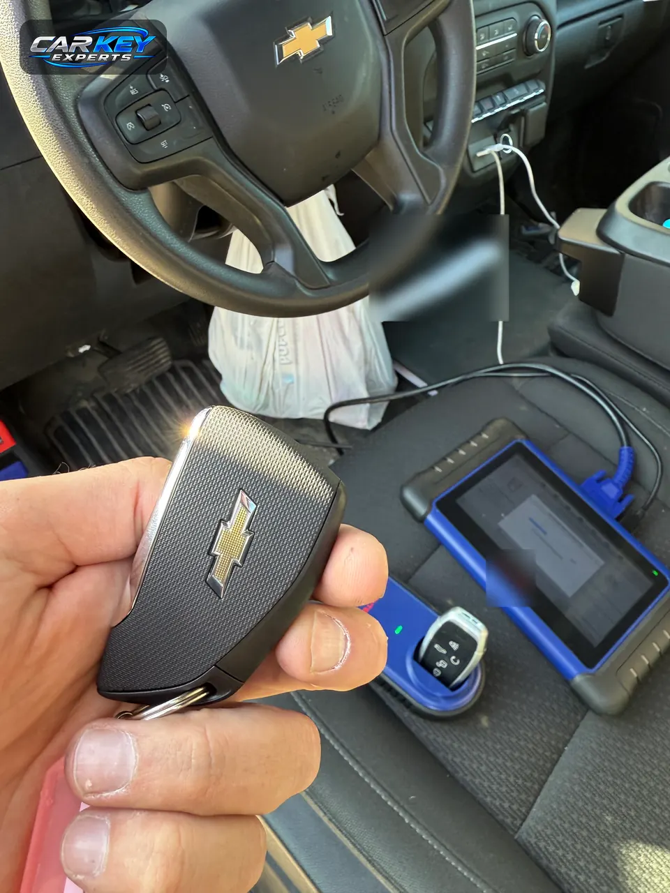 A new Chevrolet smart key held up, with the key programming equipment on the seat where it was made