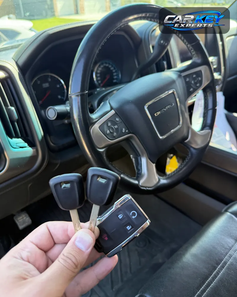 Two new chip keys and a remote held at the steering wheel of a GMC Sierra pickup