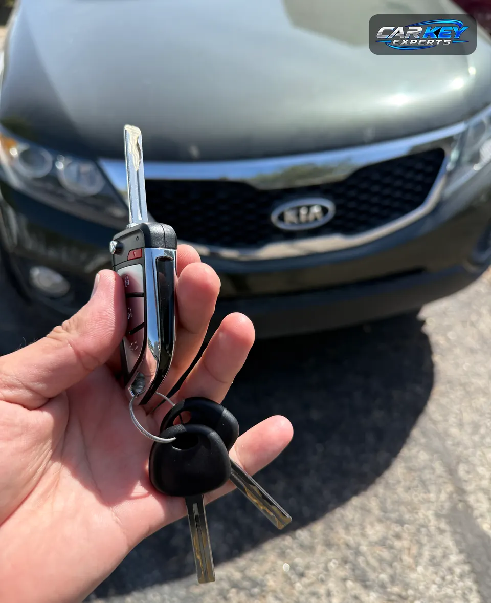 A flip key with remote buttons and two chip keys held up in front of a gray Kia in Meridian