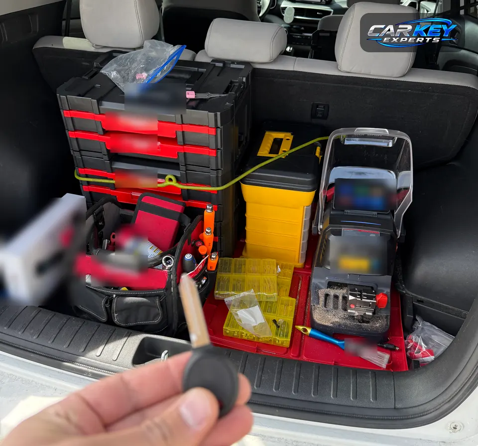 A key held up at the open hatch of an SUV whose cargo area holds a key cutting machine, key blanks and tool cases