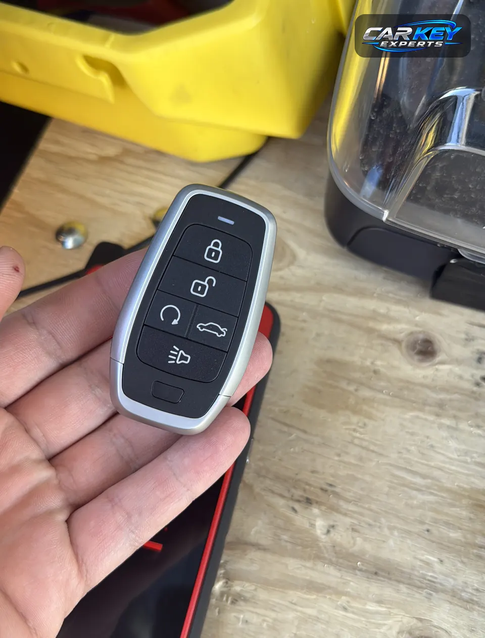 A five-button smart key with remote start, held in an open hand over a workbench