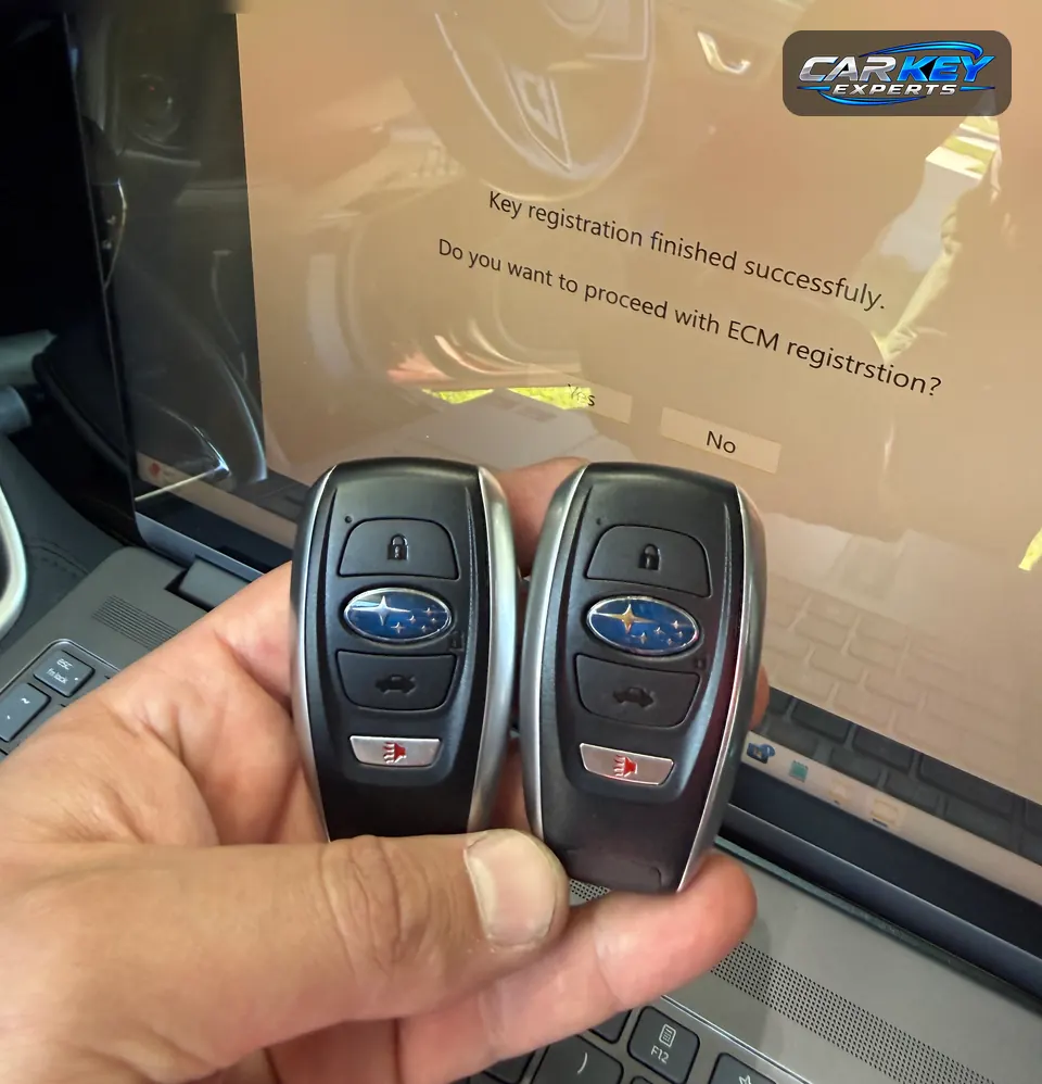 Two Subaru smart keys held up in front of a laptop screen that confirms the key registration
