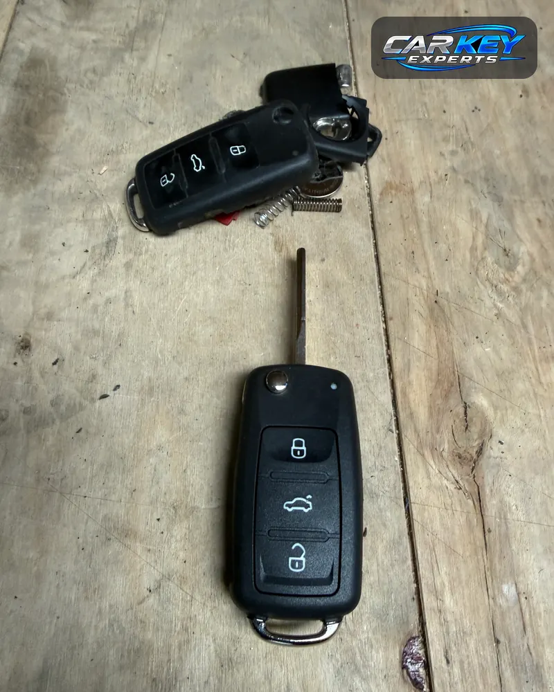 A new Volkswagen flip key below the broken original, its shell cracked and springs loose